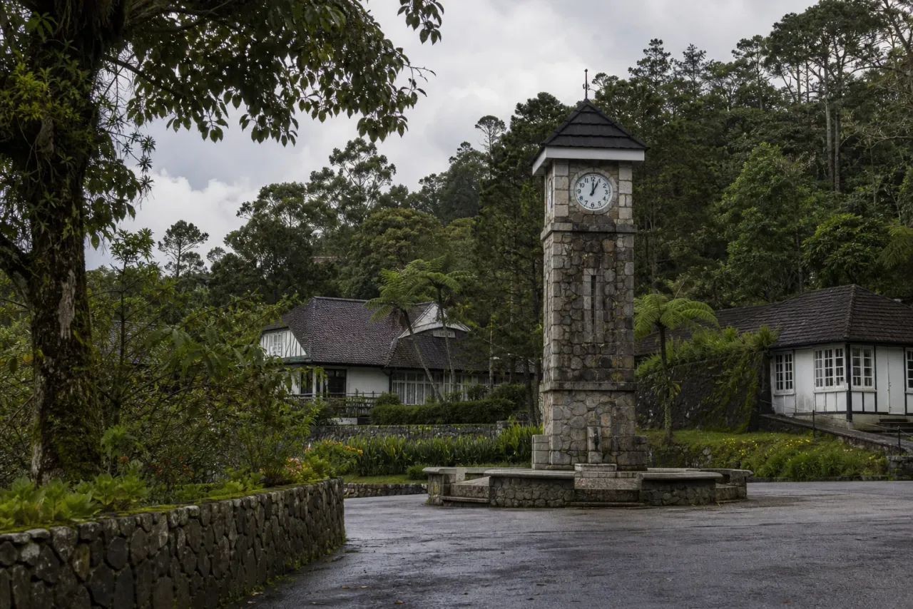 AI-created editorial interpretation of Fraser's Hill stone clock tower among damp gardens and modest highland buildings
