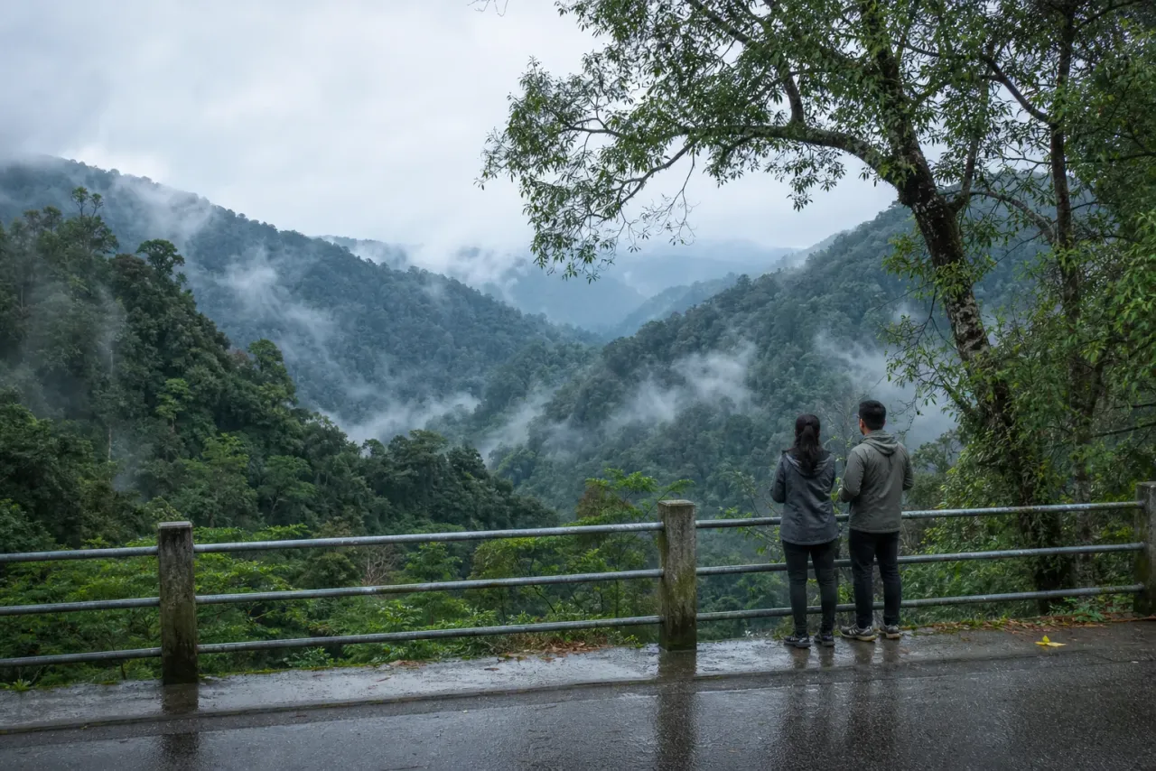 AI-created editorial view of two travellers pausing safely beside a misty tropical highland valley