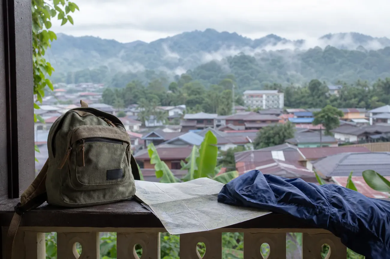 AI-generated editorial interpretation of a backpack, rain jacket and route map overlooking a Malaysian hill town