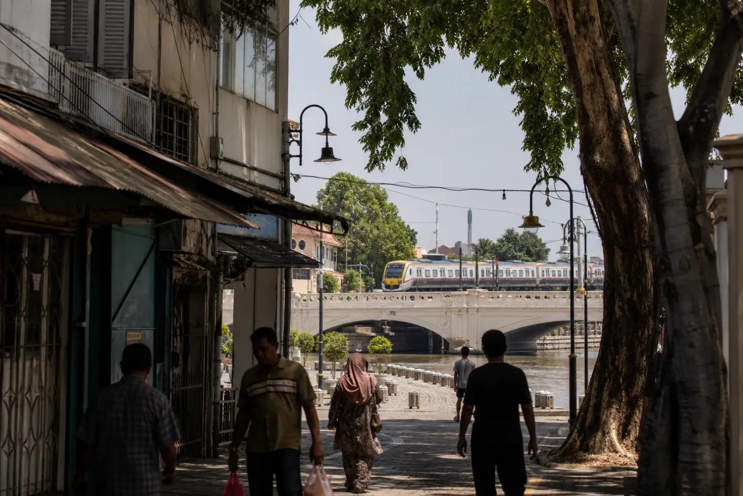 AI-created editorial interpretation of a train crossing Klang's river as pedestrians enter the old town